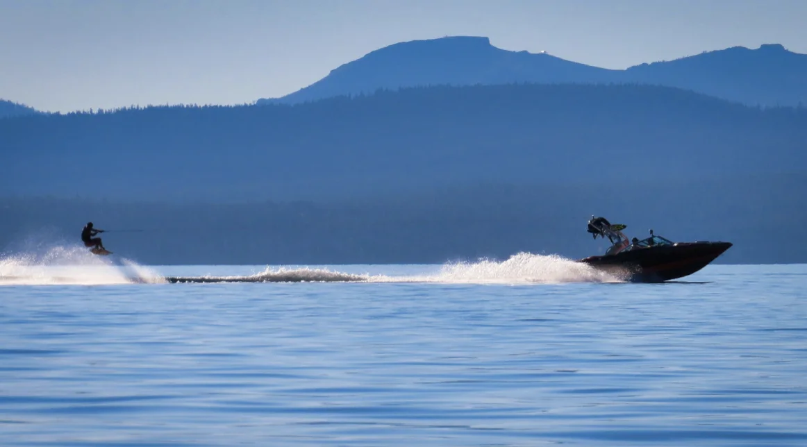 A boat pulls a water skier across a lake, with a mountain range in the background.